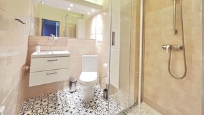 Un baño moderno con ducha de vidrio, un lavamanos blanco y un inodoro.