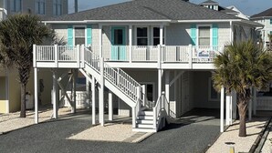 Une maison à deux étages située en bord de mer, dotée d’un balcon, d’un escalier et d’un petit espace piscine.