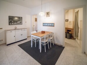 Un'area pranzo con un tavolo di legno e sedie bianche, un armadietto bianco e un tappeto nero.