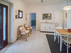 Zona pranzo con tavolo e sedie in legno, un armadietto bianco e una cornice con un'immagine appesa al muro.