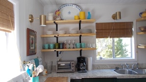 A kitchen with wooden shelves holding dishes and glasses, a toaster, and a coffee maker. - CanalHouse Private Large Home on Canal Front (Ocracoke)