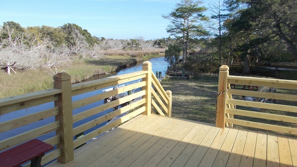 A wooden deck with a bench and a railing overlooking a river. - CanalHouse Private Large Home on Canal Front (Ocracoke)