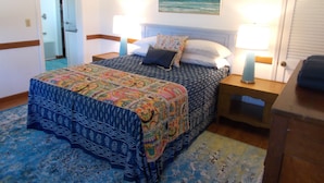A bedroom with a bed, two bedside tables, a nightstand, a door, and a painting on the wall. - CanalHouse Private Large Home on Canal Front (Ocracoke)