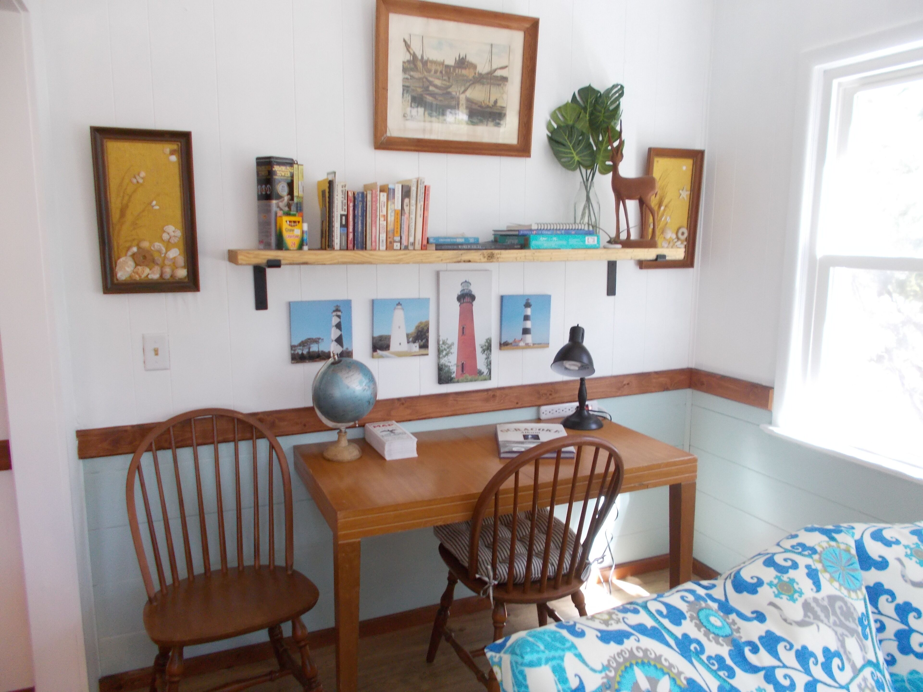A room with a wooden desk, two chairs, a globe, books, and framed pictures on the wall.