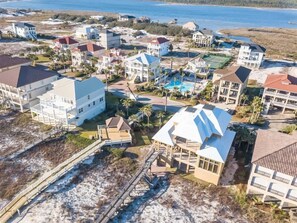 An aerial view of a coastal residential area with multiple houses, a swimming pool, and a beach access walkway.