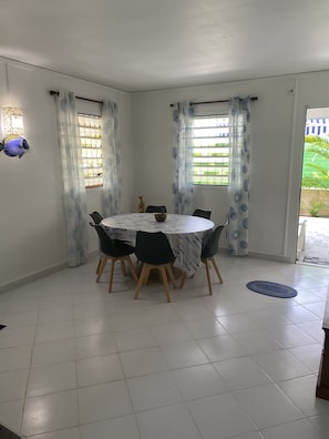 Uma sala de jantar com uma mesa redonda, cadeiras pretas e piso de azulejos brancos.