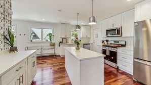 A modern kitchen with white cabinetry, a central island, stainless steel appliances, and wooden flooring. - Oakton St. Inn, Evanston near Northwestern, Loyola and Chicago (Evanston)