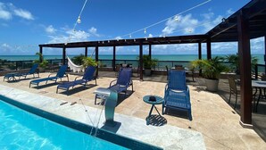 A poolside area with lounge chairs, a small table, and a hammock. - Bela Hospedagem - Marinas Cabo Branco (João Pessoa)