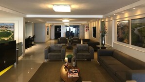 A modern lobby with a reception desk, seating area, and large framed cityscape pictures. - Bela Hospedagem - Marinas Cabo Branco (João Pessoa)