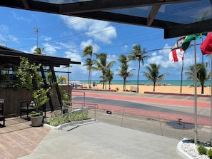 Blick auf einen Strand mit gepflastertem Weg, Palmen und blauem Himmel.