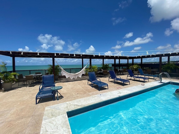 Un espace piscine avec des chaises longues, un hamac et une vue sur l’océan.
