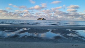 Ein Strand mit ruhigem Wasser, einer fernen Insel und einem klaren Himmel mit Wolken.