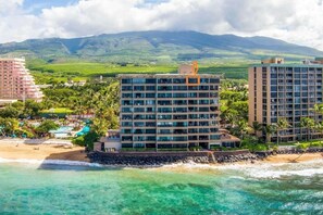 Um hotel à beira-mar com vários andares, área de piscina e vista para o oceano e montanhas ao fundo.