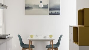 Un comedor moderno con una mesa blanca, dos sillas y un aplique de pared.