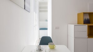 Una habitación de hotel moderna con una mesa blanca, una taza amarilla, una silla azul y una estantería.