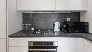 Eine Küche mit weißen Schränken, einer Marmor-Spritzschutzleiste, einem Gasherd, einer Mikrowelle und einem eingebauten Backofen.