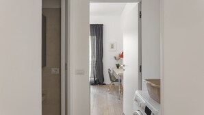 Ein Zimmer mit Waschmaschine, einer Essecke mit Tisch und Stühlen sowie einem Fenster mit Vorhängen.