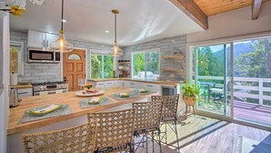 A modern kitchen with a large island, wooden ceiling, and large windows overlooking a deck. - Picturesque Cabin: 2 Balconies, Walk to Lake! (Crestline)