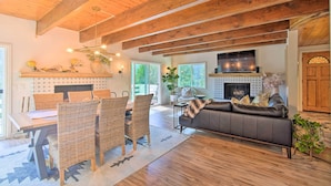 A spacious living room with a fireplace, a dining area with wicker chairs, and a large sofa. - Picturesque Cabin: 2 Balconies, Walk to Lake! (Crestline)