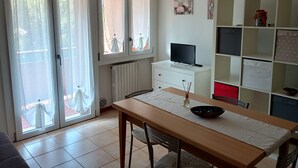 A room with a dining table, chairs, a TV on a white cabinet, and a bookshelf. - Simona apartment near Lake Garda and Verona (sona)