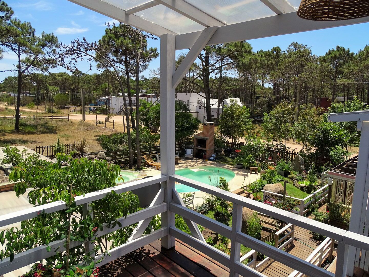 A view from a balcony overlooking a swimming pool, surrounded by greenery and a wooden deck.