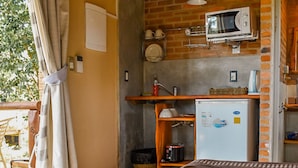 A compact room with a bed, a small kitchenette, a refrigerator, and a window with curtains. - Il Tano Suites Punta del Diablo (Punta del Diablo)