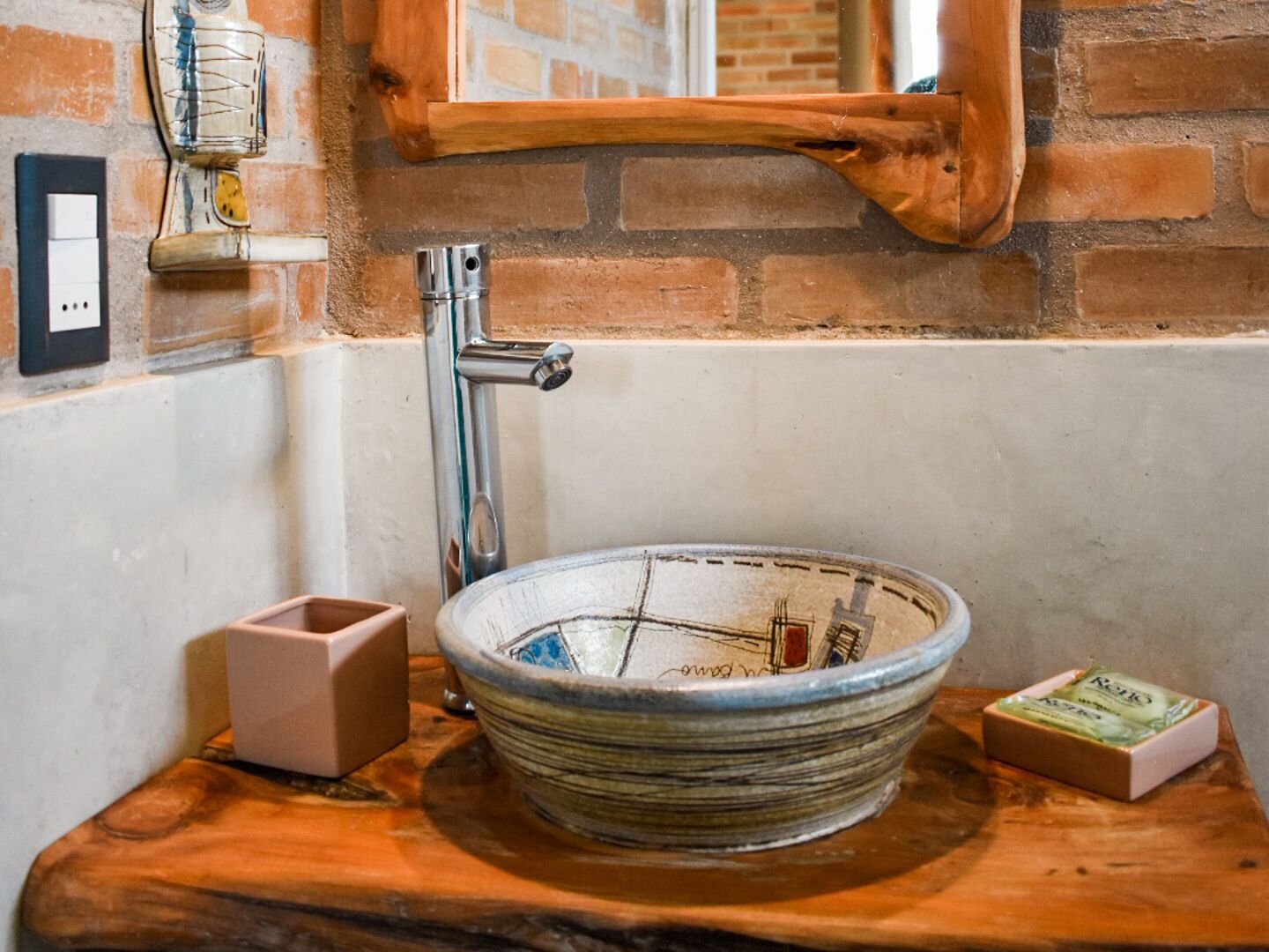 A bathroom with a round, mosaic sink, a wooden countertop, a mirror, and a brick wall.