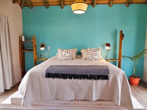 A bed with a white quilt, patterned pillows, and a black fringe throw. There are two wall-mounted lamps on either side of the bed. - Il Tano Suites Punta del Diablo (Punta del Diablo)