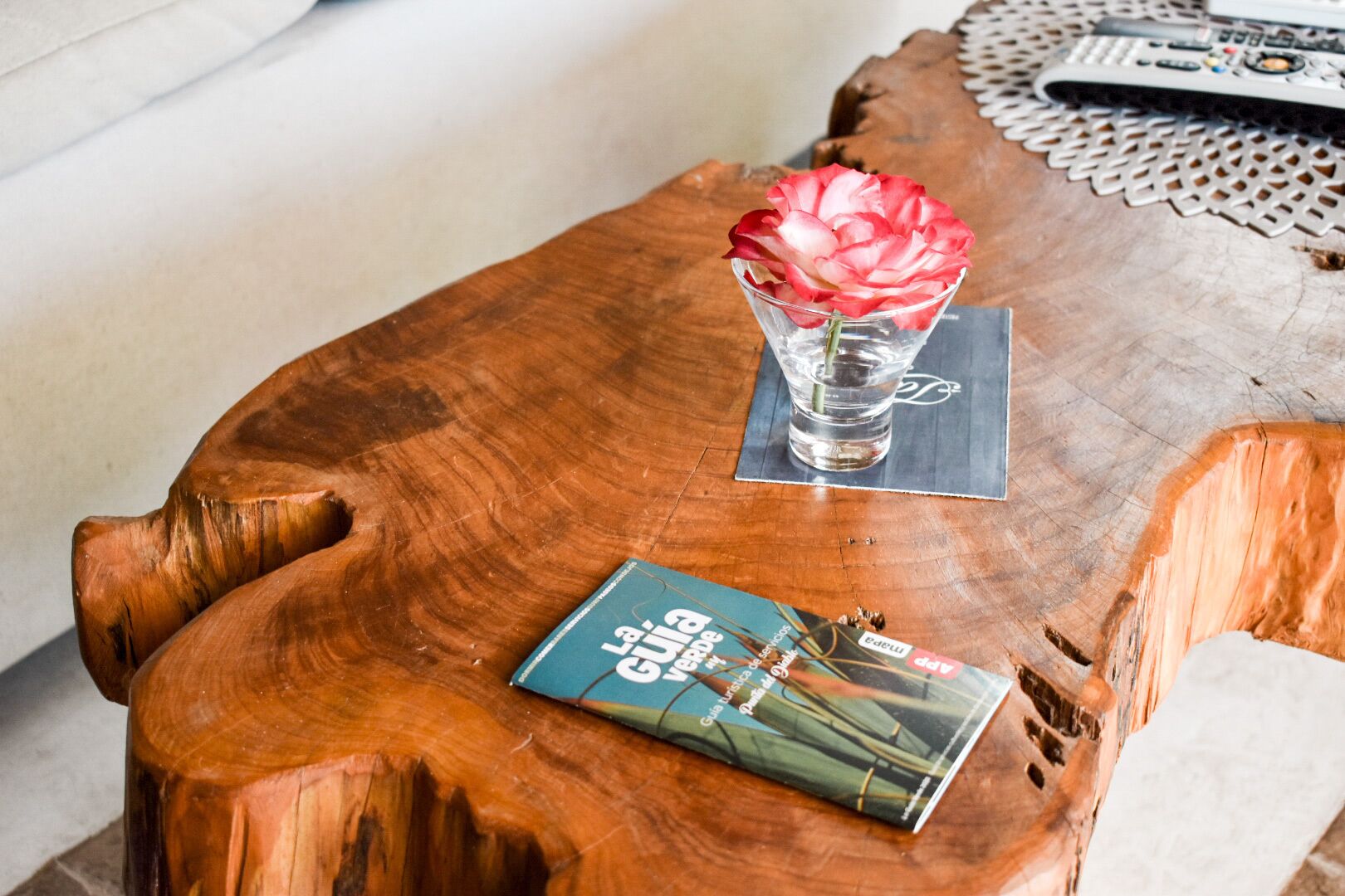 Een houten bijzettafeltje met een boek en een glazen vaas met een bloem.