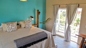 A bedroom with a bed, a hanging light fixture, a wooden headboard, a window with curtains, and a view of the outdoors. - Il Tano Suites Punta del Diablo (Punta del Diablo)