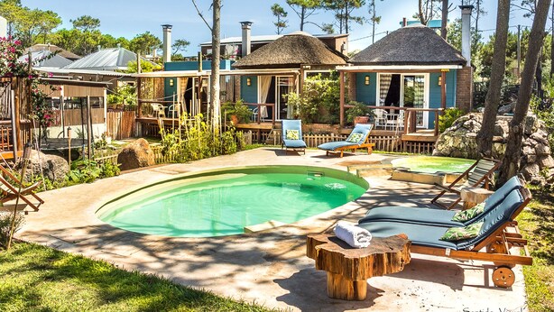 A pool area with lounge chairs and a wooden deck. - Il Tano Suites Punta del Diablo (Punta del Diablo)