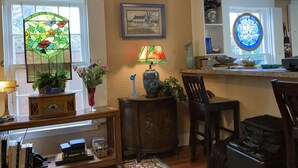 A cozy kitchen with a wooden cabinet, a dining table, chairs, a stained glass window, and a wall-mounted lamp.