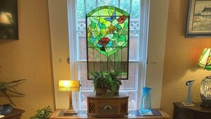 A cozy room with a stained glass window, a wooden console table with books, a vase of flowers, and a framed picture on the wall.