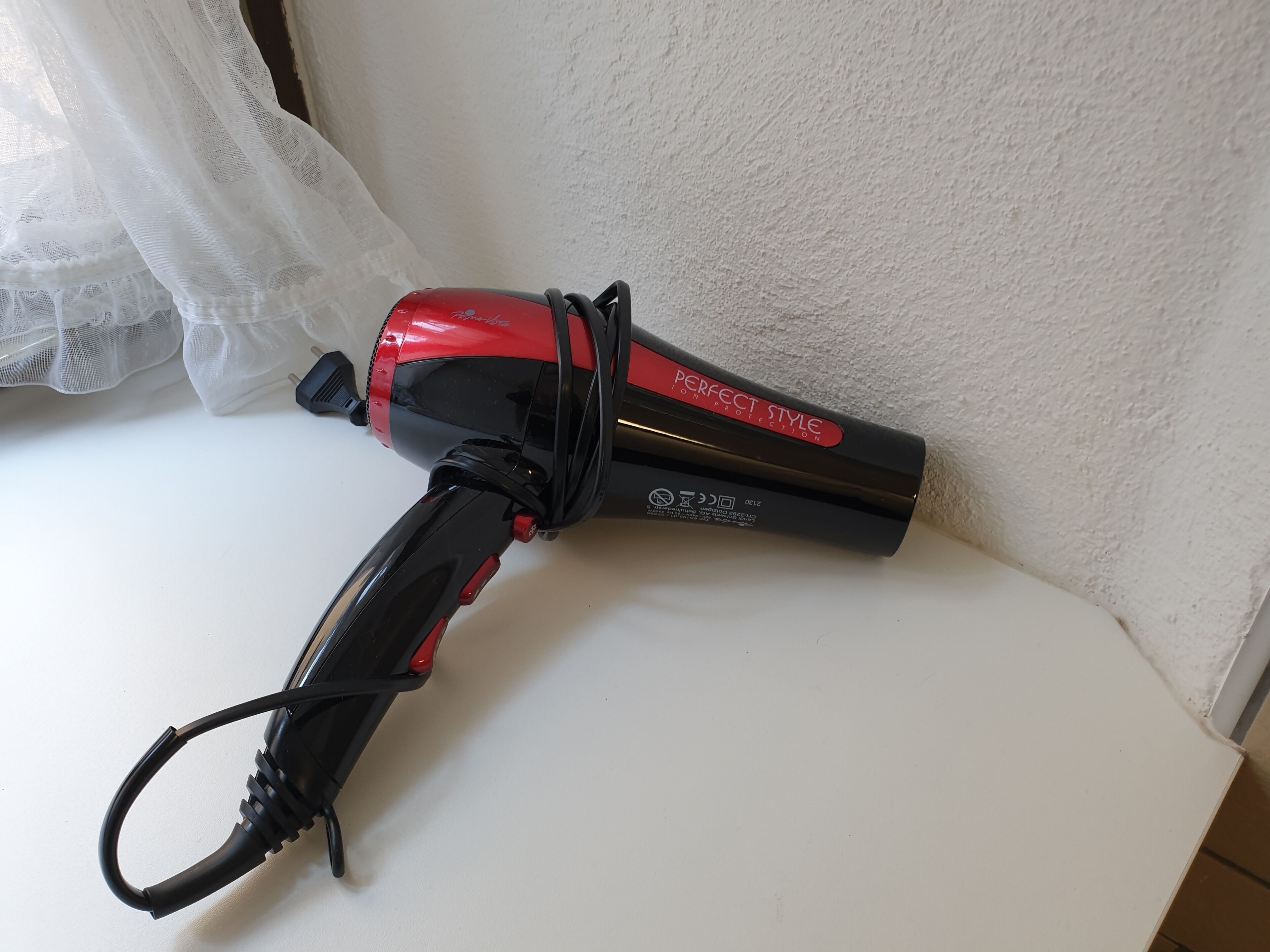 A hair dryer with a red and black design, placed on a white surface.