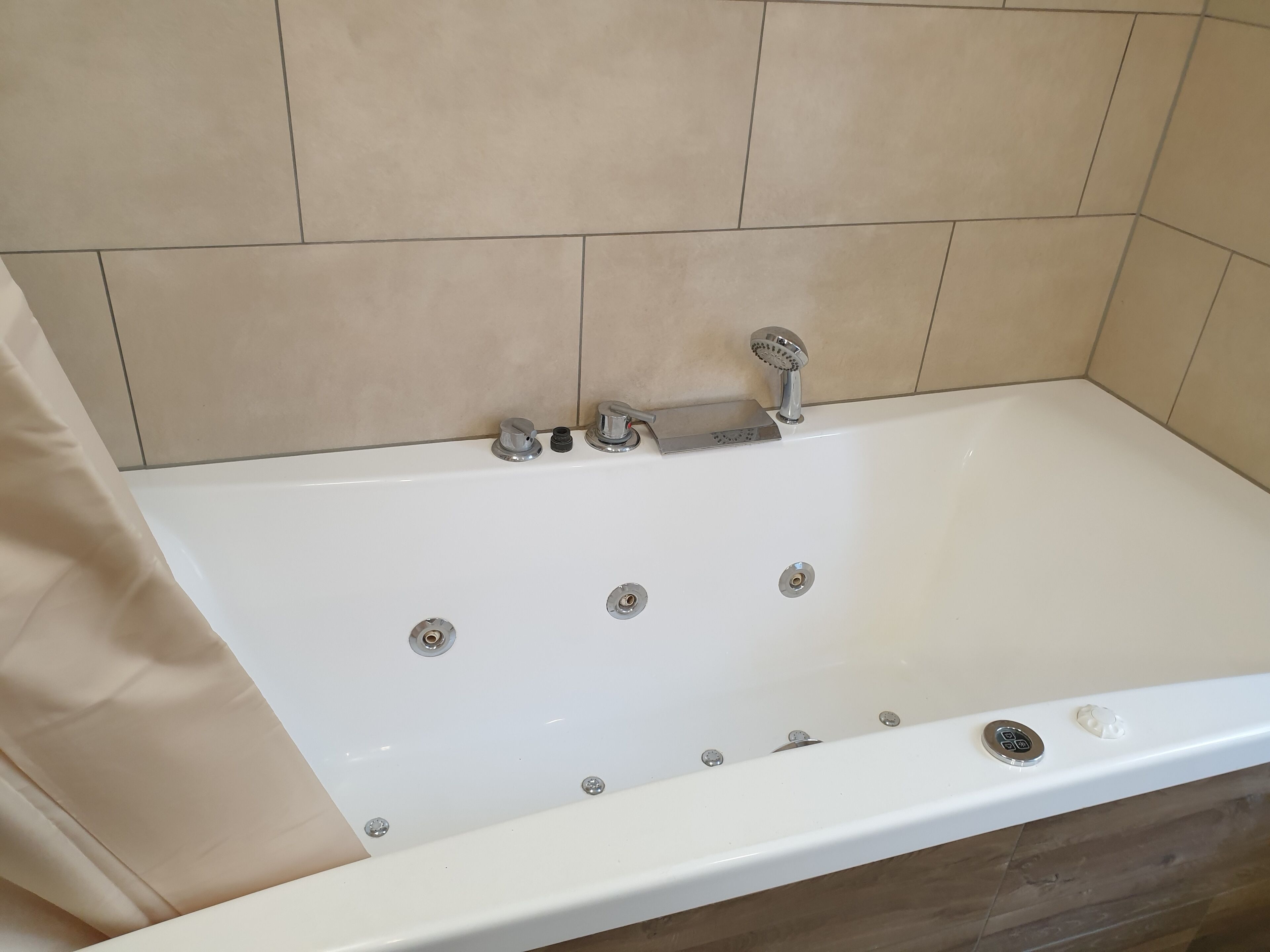Ett vitt badkar med ett handhållet duschmunstycke, en inbyggd sittplats och en kontrollpanel.