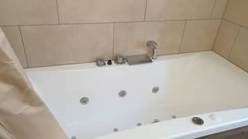 Ett vitt badkar med ett handhållet duschmunstycke, en inbyggd sittplats och en kontrollpanel.