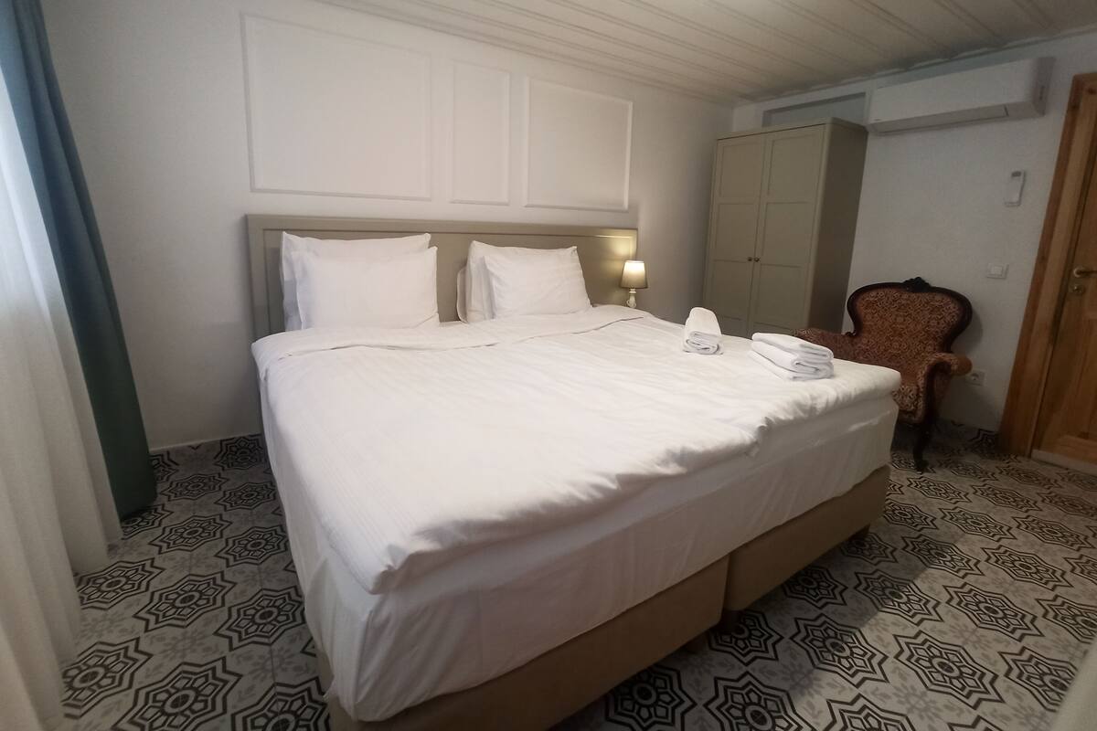 Een net opgemaakt bed met witte lakens, een hoofdeinde met twee lampen en een vloer met een patroon.