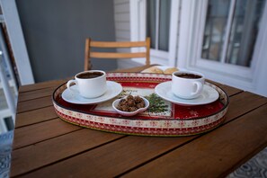 A wooden table with two white cups of coffee and a tray with cookies and a small bowl of chocolate truffles.