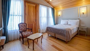 Quarto com teto de madeira, cama, cadeira, mesa e mesa de cabeceira.