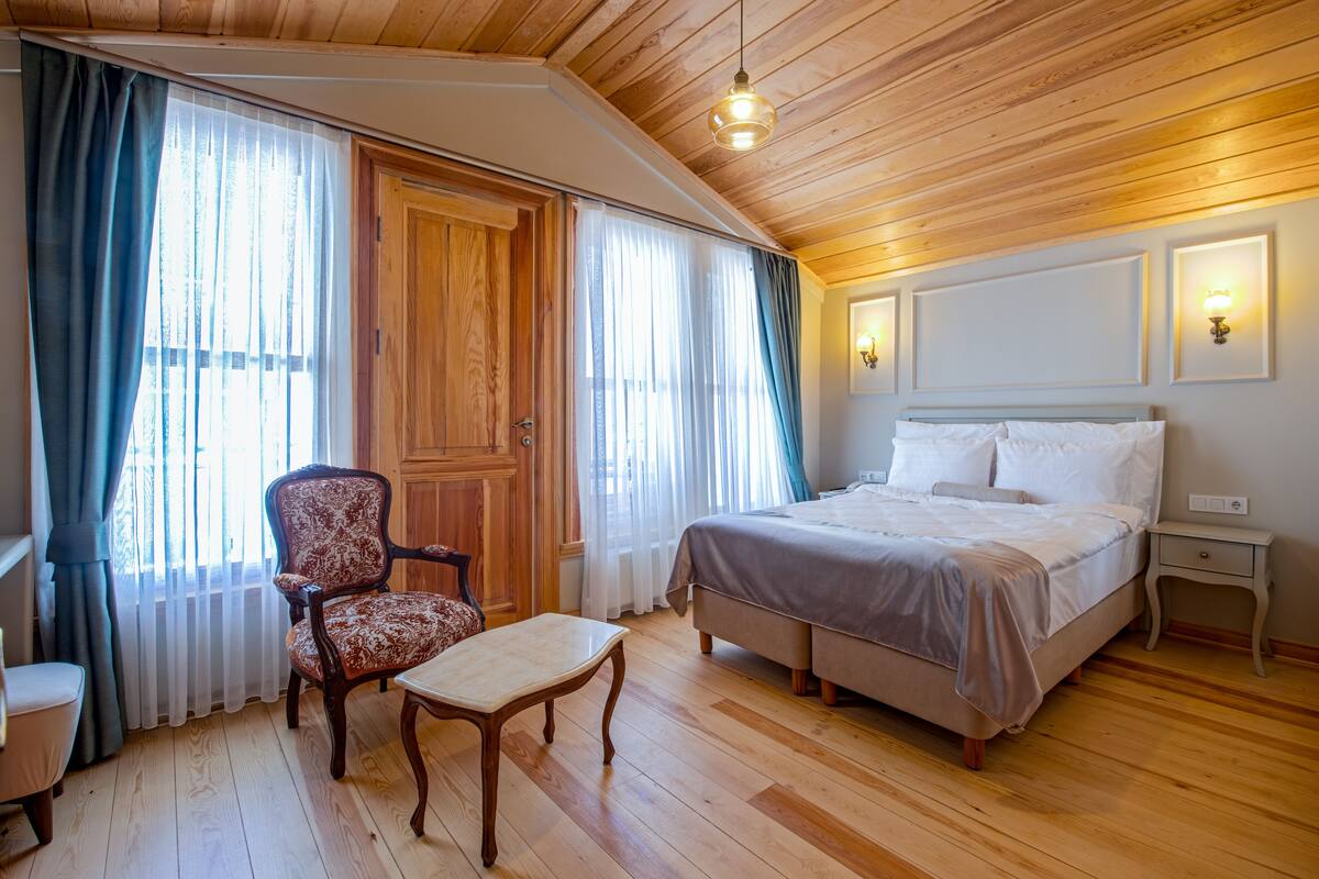 Een slaapkamer met een houten plafond, een bed, een stoel, een tafel en een nachtkastje.