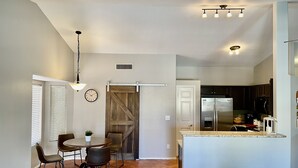 A modern kitchen with a central island, a dining area with a table and chairs, and a large sliding barn-style door. - Great location close to Downtown Gilbert! Home features pool. (Gilbert)