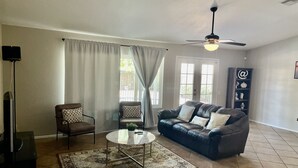 A living room with a sofa, two armchairs, a coffee table, a floor lamp, and a ceiling fan. - Great location close to Downtown Gilbert! Home features pool. (Gilbert)