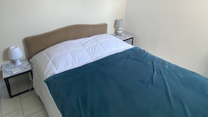Une chambre d’hôtel simple, avec un lit, une table de chevet, une lampe et un mur.