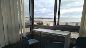 Un balcon avec une table et deux chaises, donnant sur une plage et un port de plaisance.