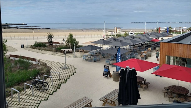Un espace extérieur aménagé avec des tables et des parasols, donnant sur une plage.