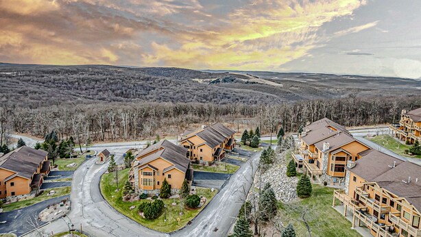 A residential area with detached houses, a winding road, and a backdrop of hills and trees. - Cozy Luxury Almost Ski-in Ski-out with Hot Tub in Southwind! (Seven Springs)