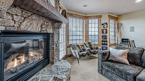 A cozy living room with a stone fireplace, comfortable seating, and large windows. - Cozy Luxury Almost Ski-in Ski-out with Hot Tub in Southwind! (Seven Springs)