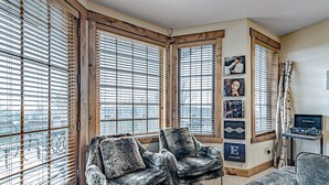 A cozy room with large windows, two plush armchairs, a small table, and a wall-mounted TV. - Cozy Luxury Almost Ski-in Ski-out with Hot Tub in Southwind! (Seven Springs)