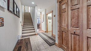 A hallway with a carpeted staircase, wooden doors, and framed pictures on the wall. - Cozy Luxury Almost Ski-in Ski-out with Hot Tub in Southwind! (Seven Springs)