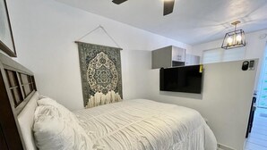 A bedroom with a bed, a mounted TV, a ceiling fan, and a patterned tapestry.